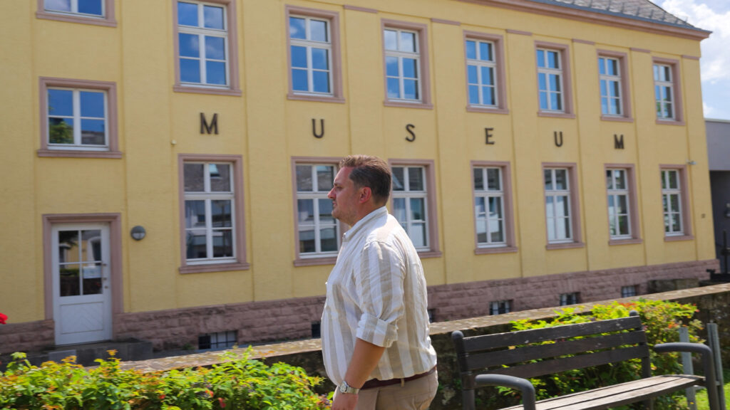 Dr. Johannes Zierden geht an einem historischen, gelben Museumsgebäude mit dem Schriftzug „Museum" vorbei.