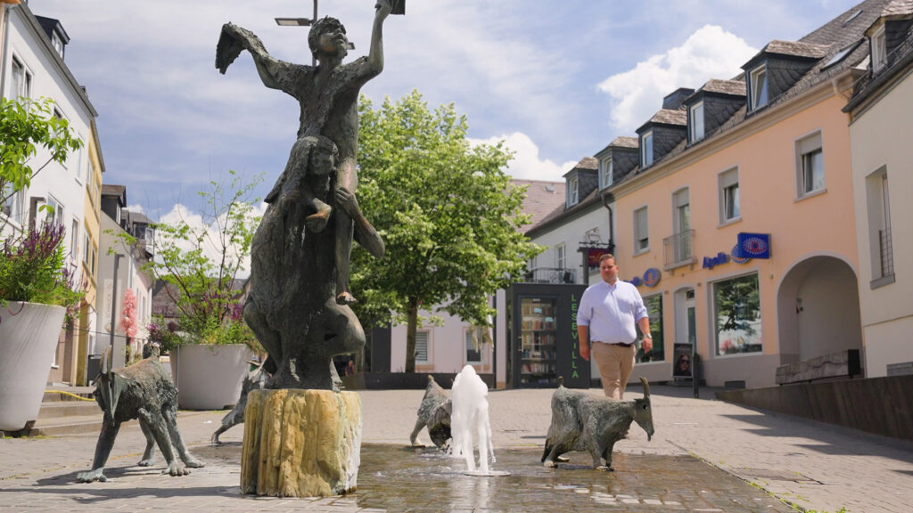 Bronzebrunnen mit Figuren- und Ziegengruppe in der Bitburger Innenstadt, im Hintergrund Dr. Johannes Zierden.