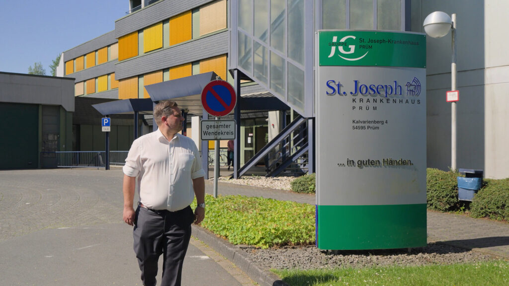 Dr. Johannes Zierden vor dem St.-Joseph-Krankenhaus Prüm neben dem Eingangsschild.